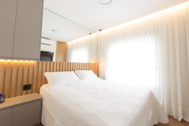 Suíte de casal com cabeceira estofada e iluminação suave em apartamento reformado em São Paulo